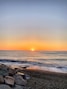 the sun is setting over the ocean on a rocky beach