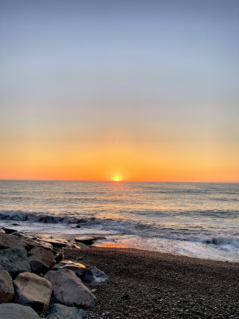 El sol se está poniendo sobre el océano en una playa rocosa