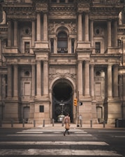 a man walking across a street in front of a large building