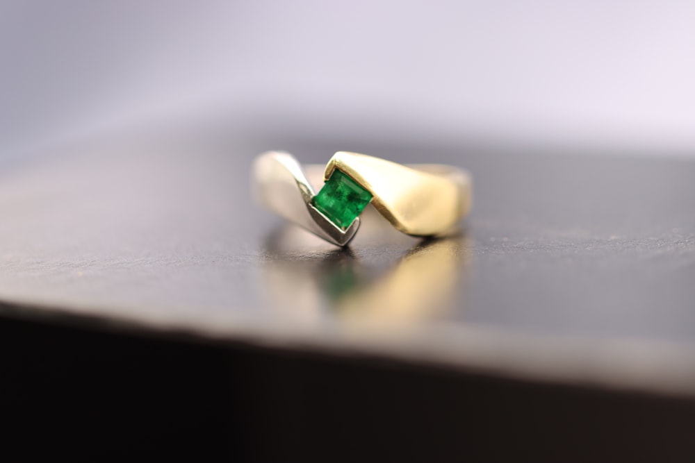 Un anillo de oro con una piedra verde sentado sobre una mesa