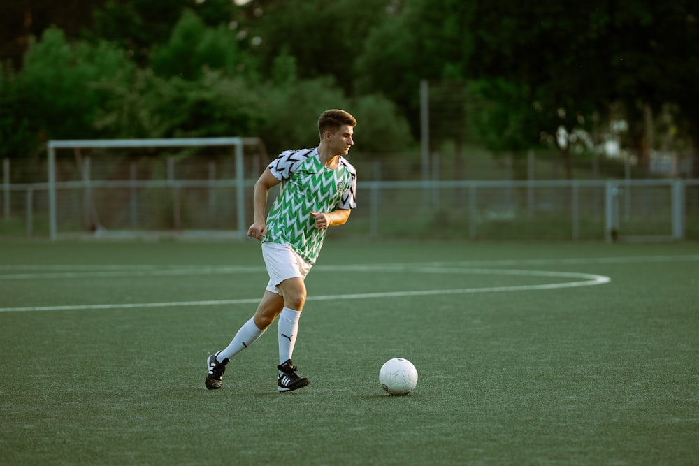 um homem de camisa verde e branca está chutando uma bola de futebol