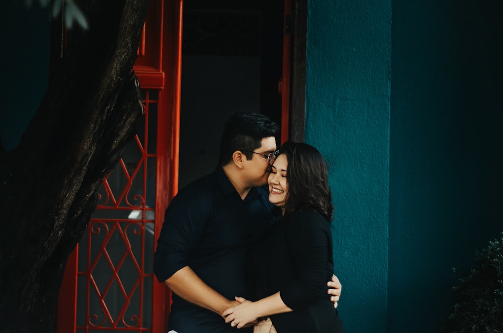 a man and a woman embracing in front of a red door