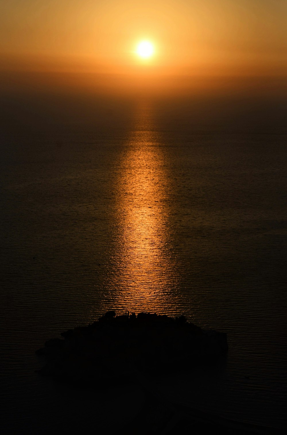 the sun is setting over the ocean with a small island in the foreground