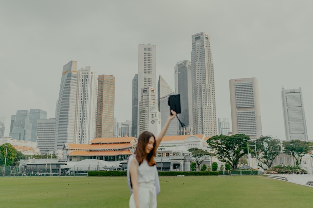 a woman in a white dress holding up a black object in front of a city