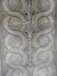 Intricate grey stone or metal embossing with symmetrical, repeating circular and curved patterns adorned with textured surfaces.