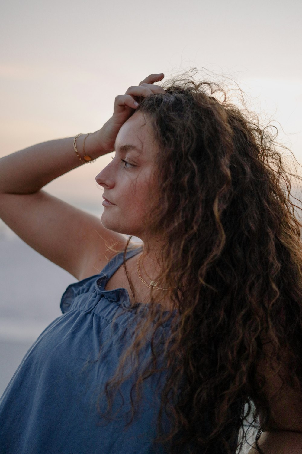 a woman with long curly hair standing near the ocean
