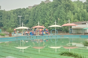 Community facilities including a swimming pool and playground surrounded by trees at Vinhomes Ha Long Xanh.