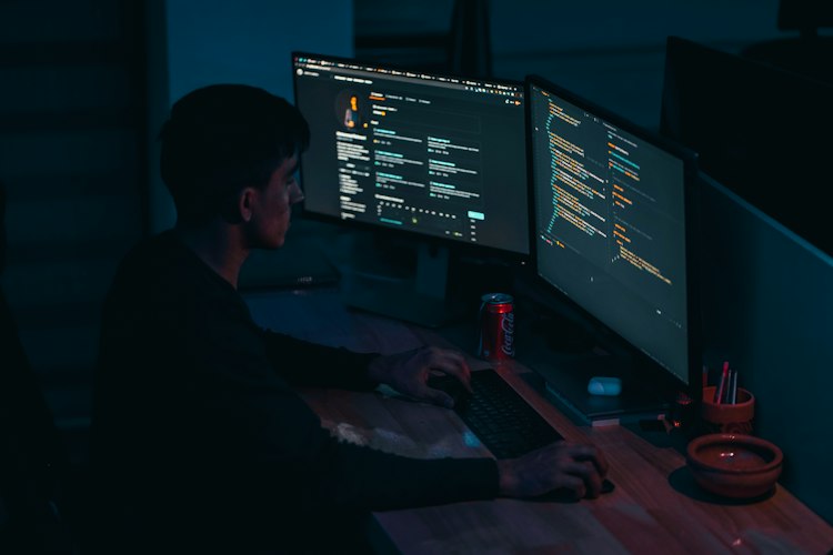 Close-up of hands typing on a keyboard with lines of code visible on the monitor