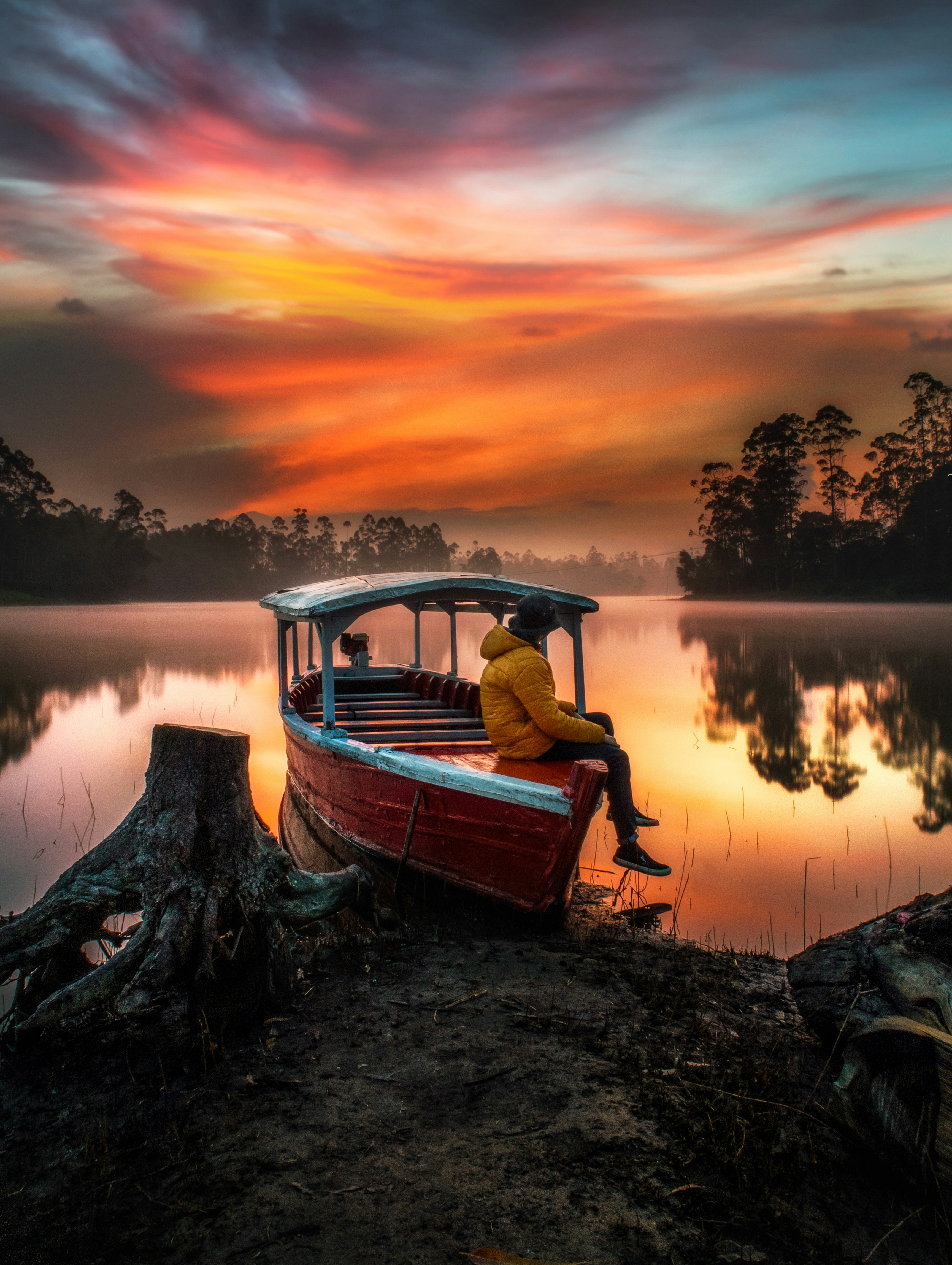 homme en chemise rouge assis sur le bateau pendant le coucher du soleil