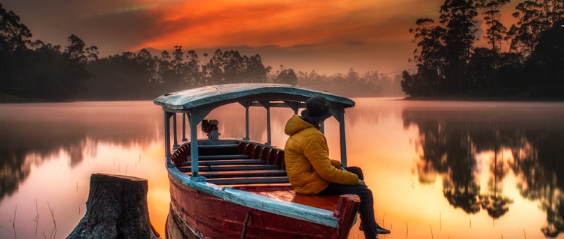 man in red shirt sitting on boat during sunset