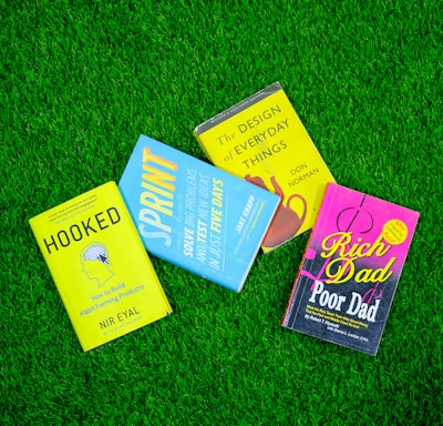a group of three books laying on top of a lush green field