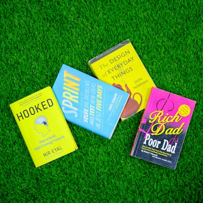 a group of three books laying on top of a lush green field