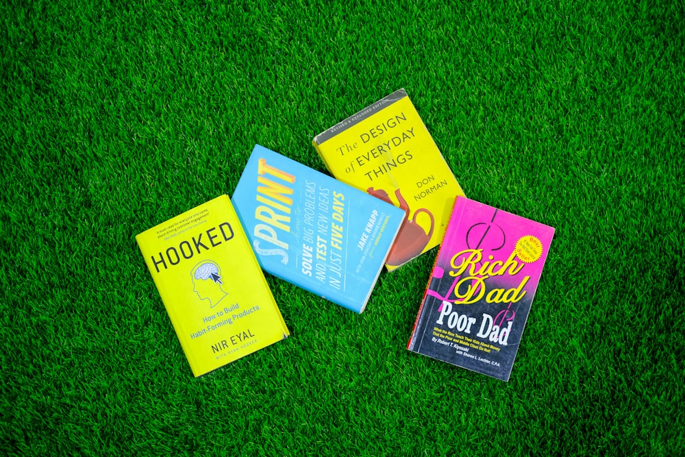 a group of three books laying on top of a lush green field