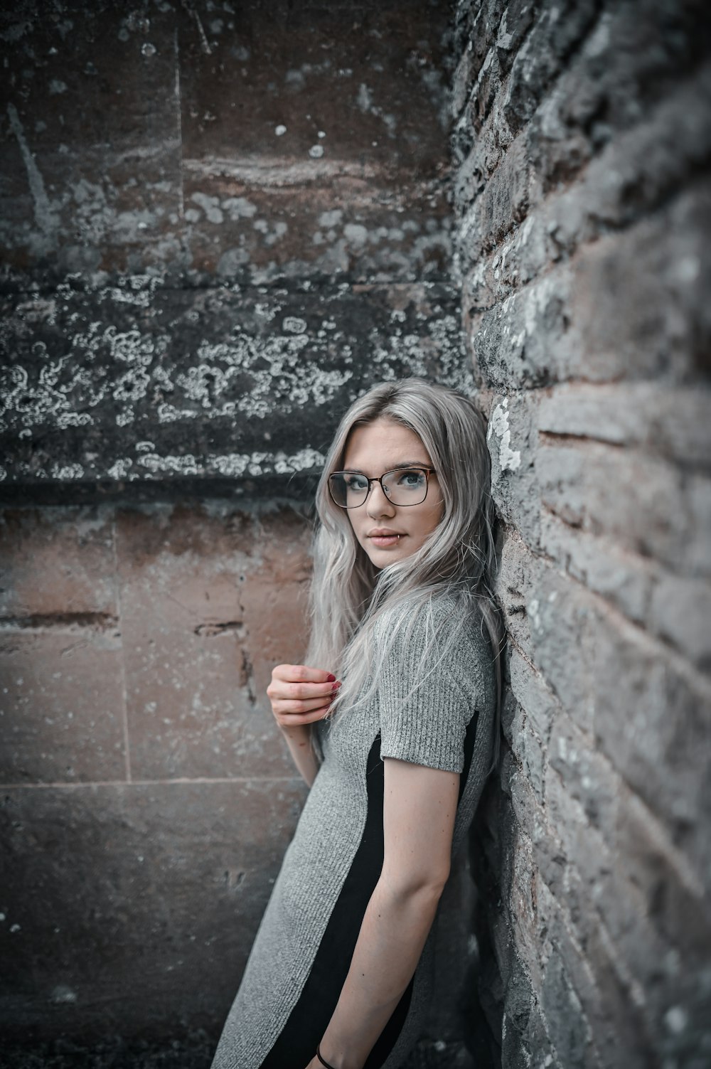 woman in gray knit sweater leaning on brown brick wall