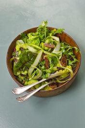a wooden bowl filled with a salad and two spoons