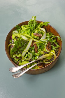 a wooden bowl filled with a salad and two spoons