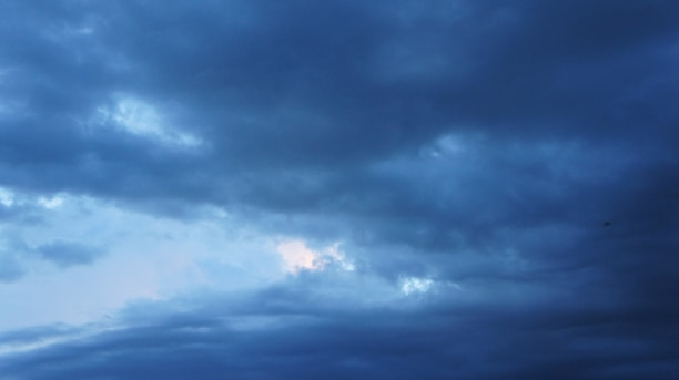 Dark, thick clouds dominate the sky, with a small patch of lighter blue indicating a break in the clouds. The atmosphere is heavy and moody, suggesting an impending storm.