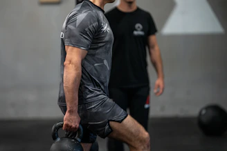 Man lifting kettlebell with trainer watching