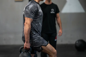 Man lifting kettlebell with trainer watching