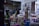 An art studio filled with easels, stools, and various painting supplies. The walls display sketches and busts, creating an atmosphere of creativity and learning. A tripod and several colorful plastic stools are scattered across the room. A large window with a curtain lets in natural light.