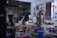 An art studio filled with easels, stools, and various painting supplies. The walls display sketches and busts, creating an atmosphere of creativity and learning. A tripod and several colorful plastic stools are scattered across the room. A large window with a curtain lets in natural light.