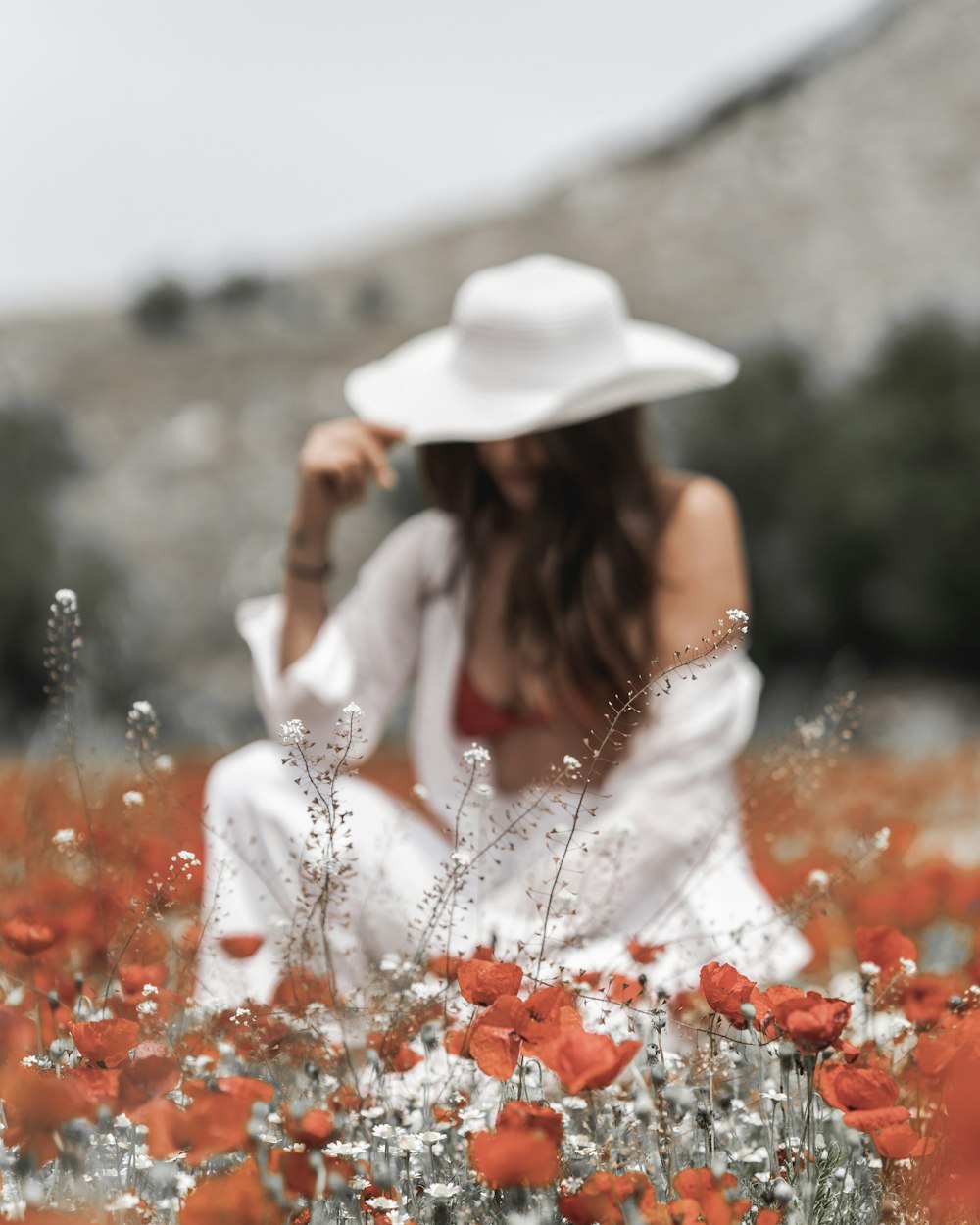 a woman wearing a white hat sitting in a field of flowers