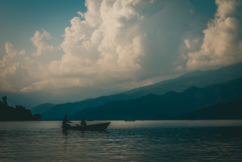 a man in a boat on a lake under a cloudy sky