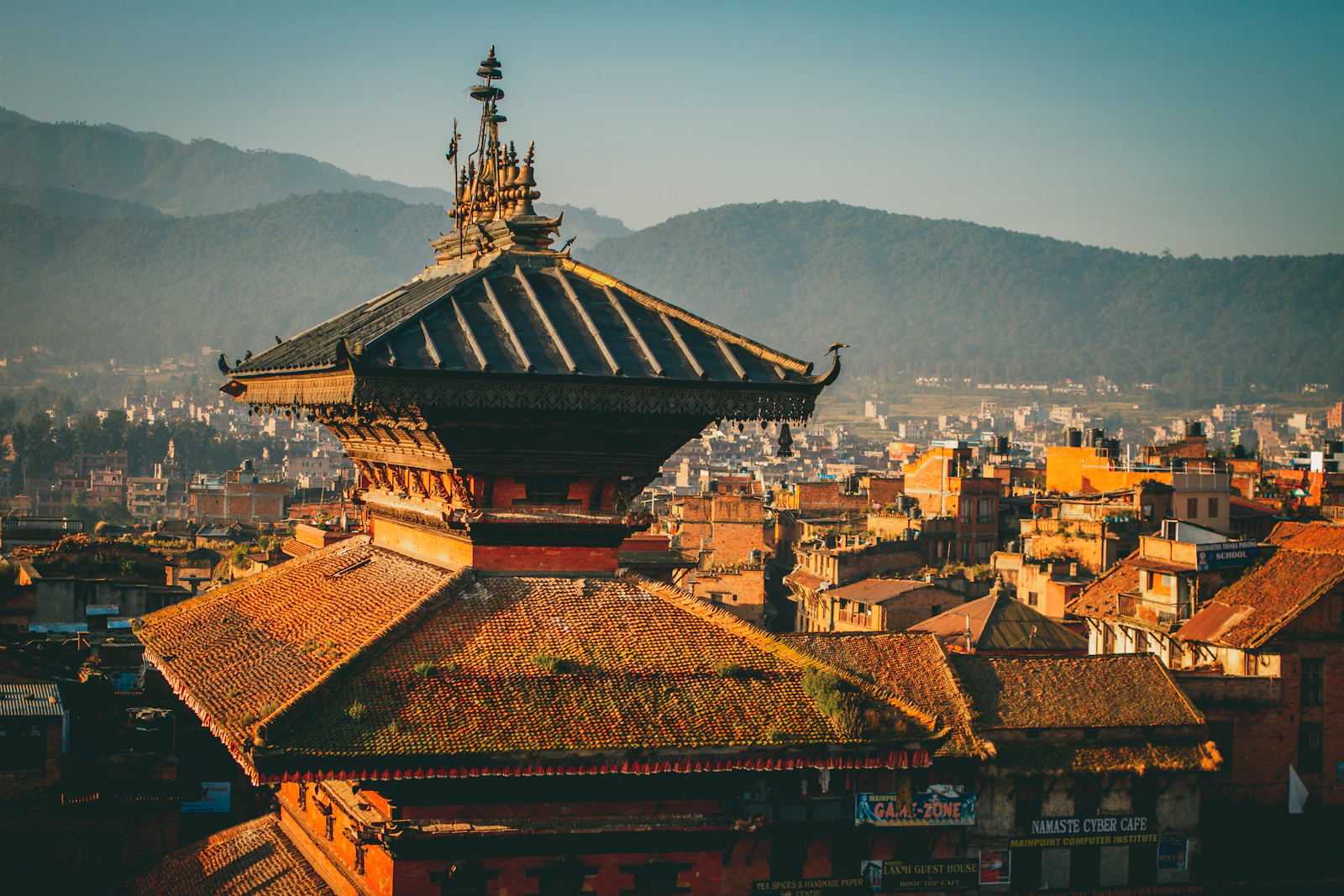 A tiered Newar pagoda rising above Bhaktapur's tiled rooftops with the valley hills behind in golden light