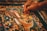 A detailed painting featuring intricate patterns and ornate designs is being meticulously created. The artwork includes mythical creatures, swirling motifs, and vibrant colors. A hand delicately holds a fine paintbrush, applying careful strokes to add detail to the central dragon-like figure.