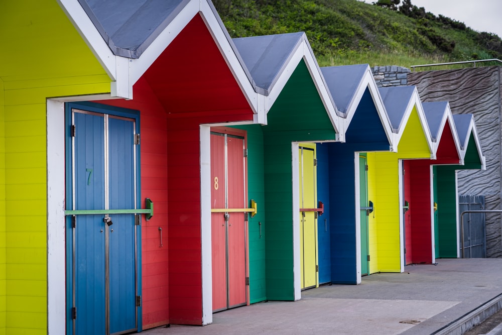 a row of brightly colored beach huts next to a hill