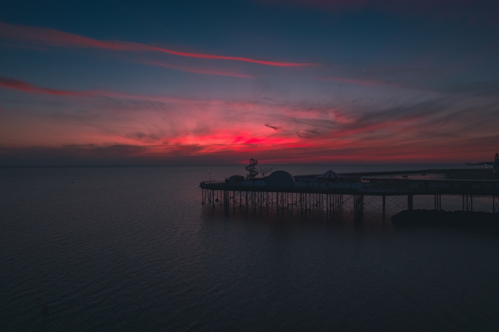 the sun sets over a pier in the ocean