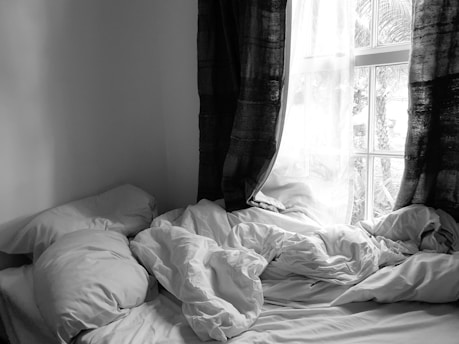 grayscale photo of bed with white blanket