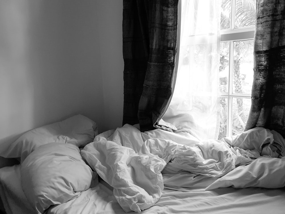 Foto en escala de grises de la cama con una manta blanca