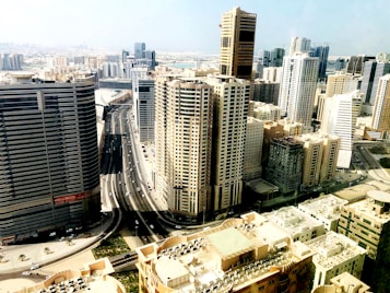 A bustling urban skyline filled with tall skyscrapers, intricate highways, and buildings of varying heights and designs. The cityscape is expansive, showcasing modern architecture and a clear sky that hints at a bright day.