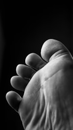 A close-up black and white photograph of the underside of a foot, focusing on the toes. The texture of the skin is visible, showing the natural curves and creases.