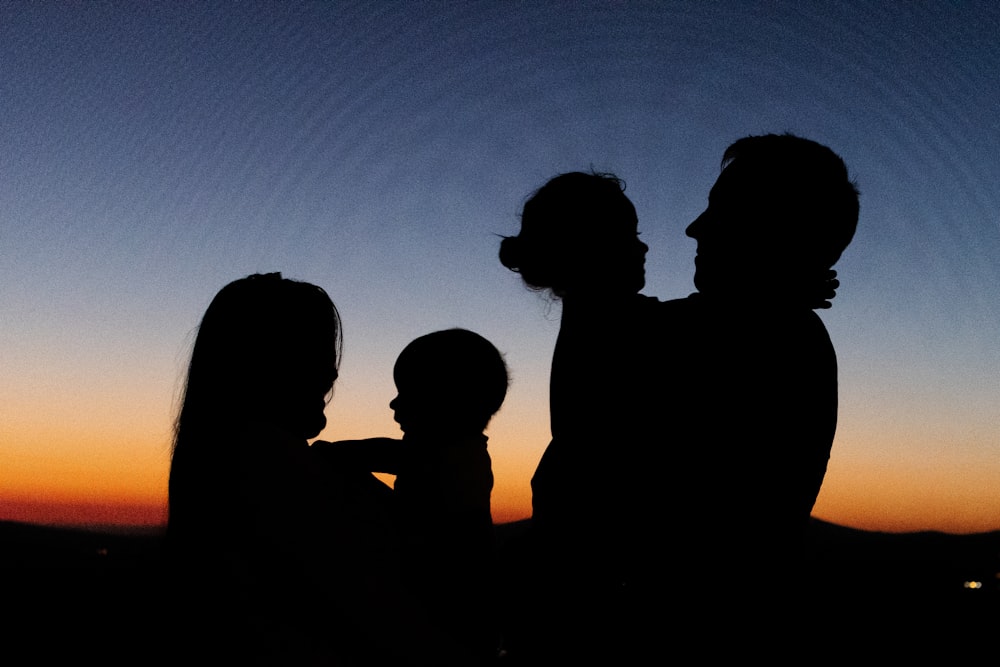 silhouette of 2 women and man standing during sunset