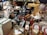 A collection of various vintage objects including cameras, bronze sculptures, picture frames, a stack of books, ornate jars, and busts are arranged on a table. The items are diverse, ranging from decorative to utilitarian, and create a sense of an antique market or collection.