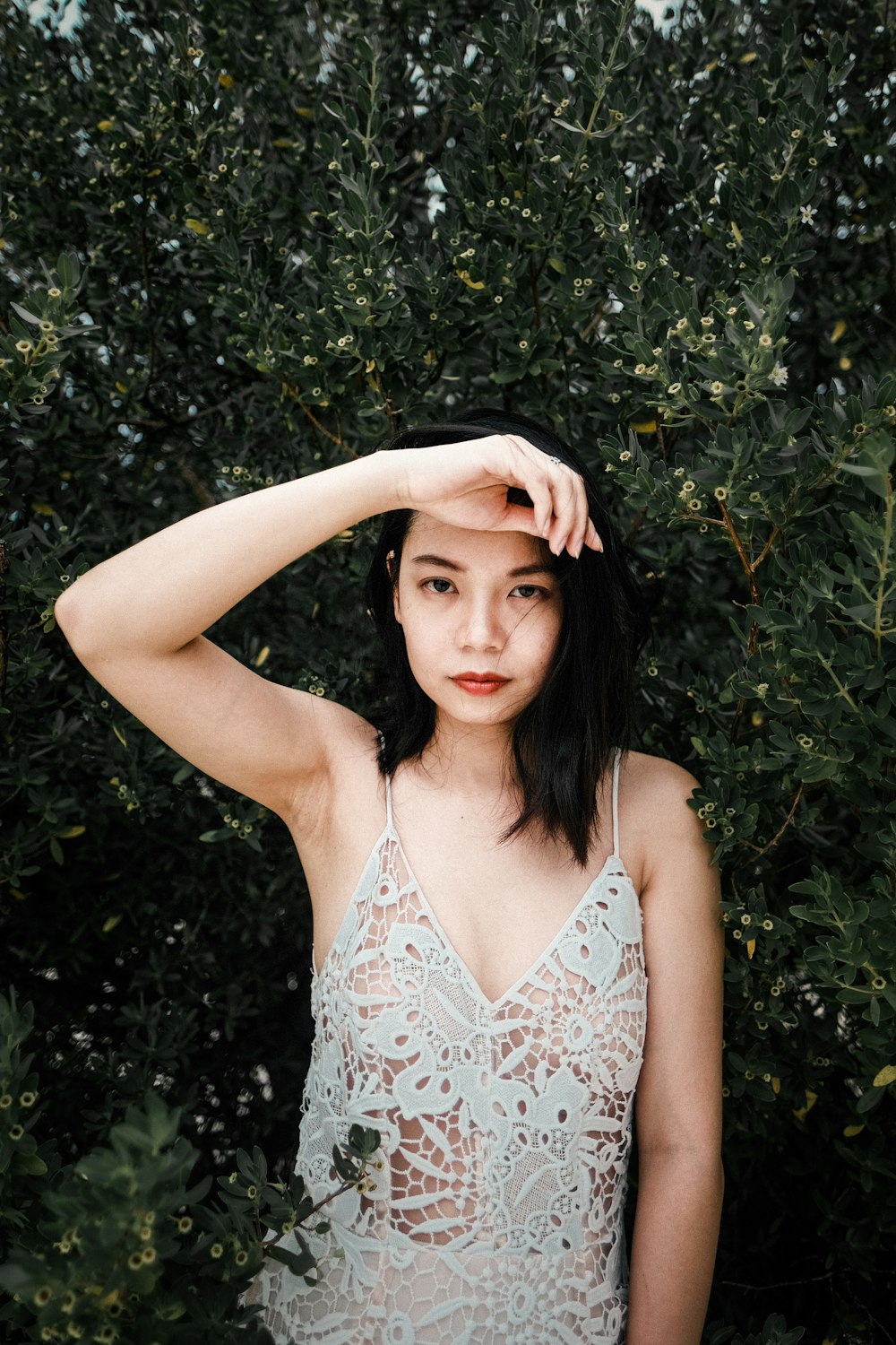 a woman standing in front of a bush with her hand on her head