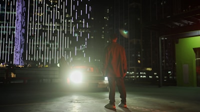 A locksmith technician unlocking a car door at night with bright city lights in the background