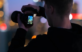 man in black jacket taking photo of city lights during night time