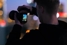 man in black jacket taking photo of city lights during night time