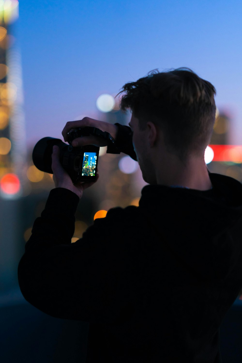 夜の街の明かりの写真を撮る黒いジャケッ��トの男性