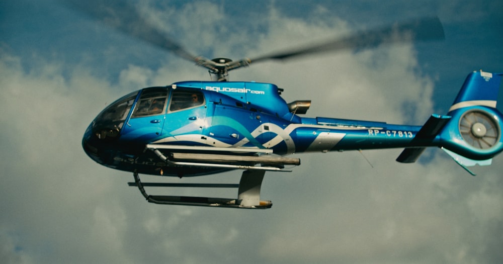 a blue helicopter flying through a cloudy sky