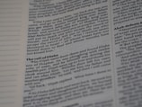 A close-up shot of an open book showing text in two columns. The text appears to be printed with black ink on white paper. The left margin contains lines for notes, and the text is organized with headings and paragraphs, typically seen in a textbook or scripture.