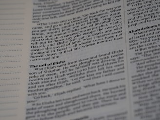 A close-up shot of an open book showing text in two columns. The text appears to be printed with black ink on white paper. The left margin contains lines for notes, and the text is organized with headings and paragraphs, typically seen in a textbook or scripture.