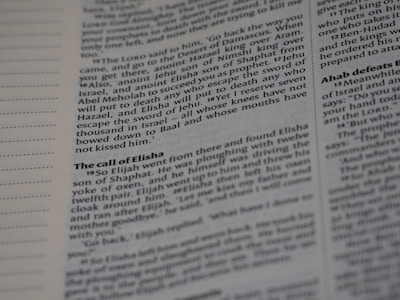 A close-up shot of an open book showing text in two columns. The text appears to be printed with black ink on white paper. The left margin contains lines for notes, and the text is organized with headings and paragraphs, typically seen in a textbook or scripture.