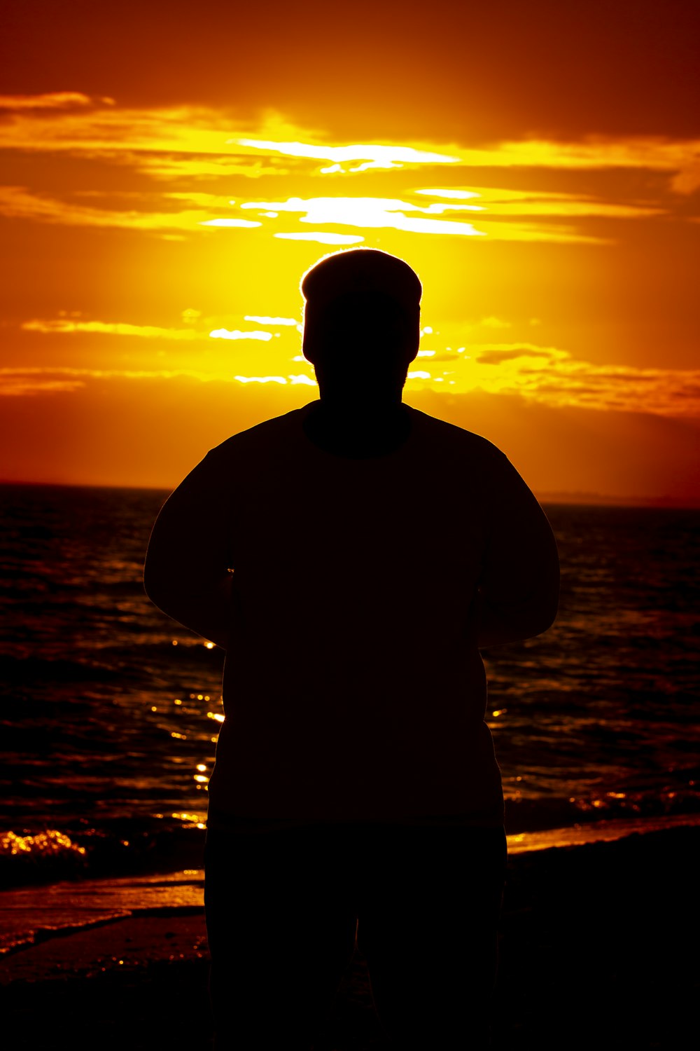 silhouette of man standing near body of water during sunset