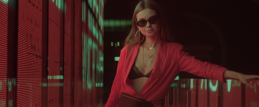 a woman in a red jacket and sunglasses standing in a hallway