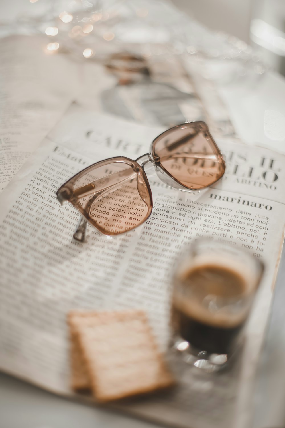 a pair of glasses sitting on top of a newspaper next to a cup of coffee