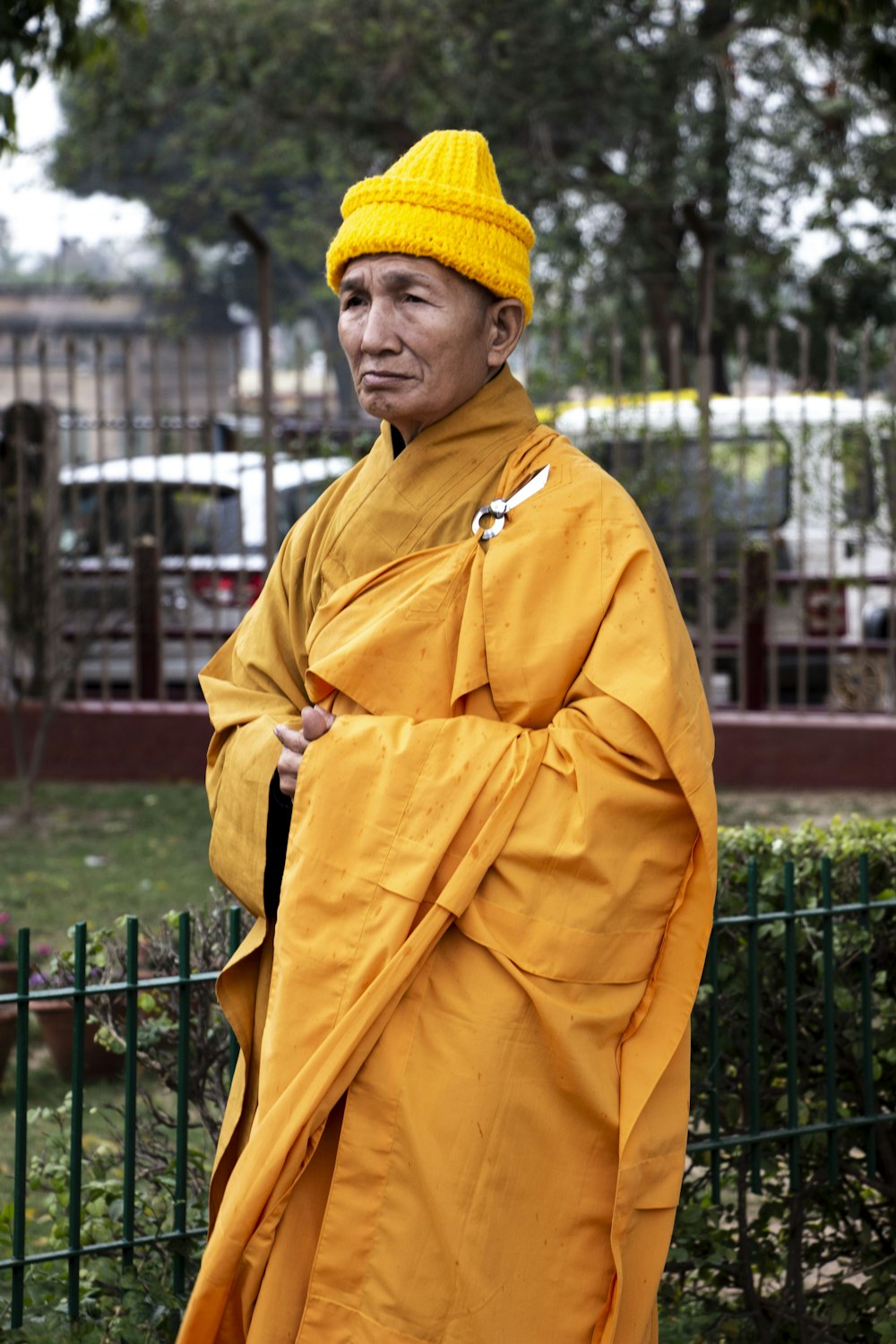 Hombre con camisa de vestir amarilla y gorra de punto azul de pie cerca de la valla